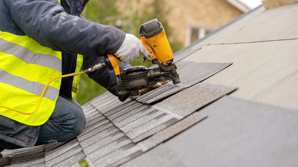 Workman using pneumatic nail gun install tile on roof of new house under construction